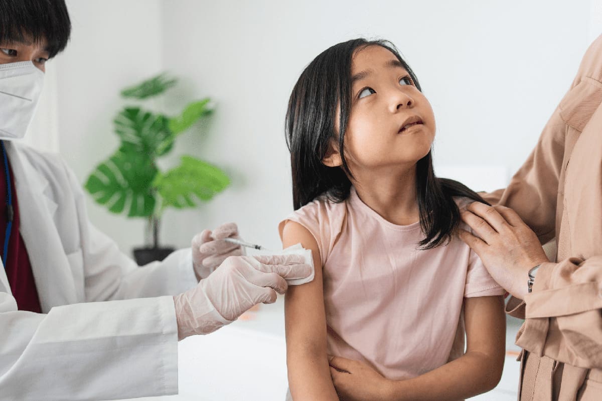 A little girl getting a vaccine shot in her arm while her mother supports her in the process