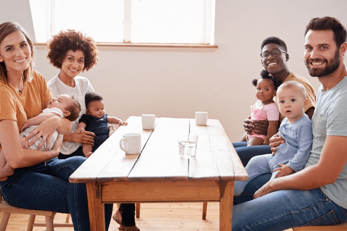 Portrait Of Two Families With Babies Meeting Around Table On Play Date At Home