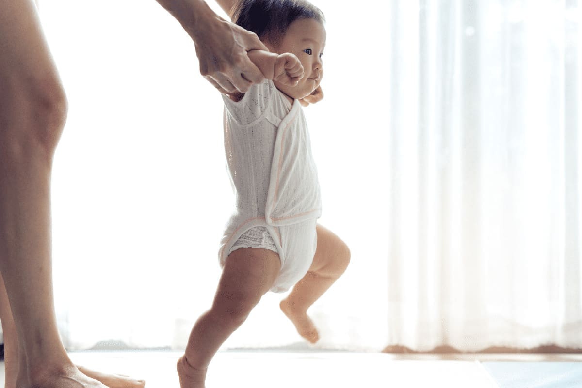 Asian baby taking first steps walk forward on the soft mat.