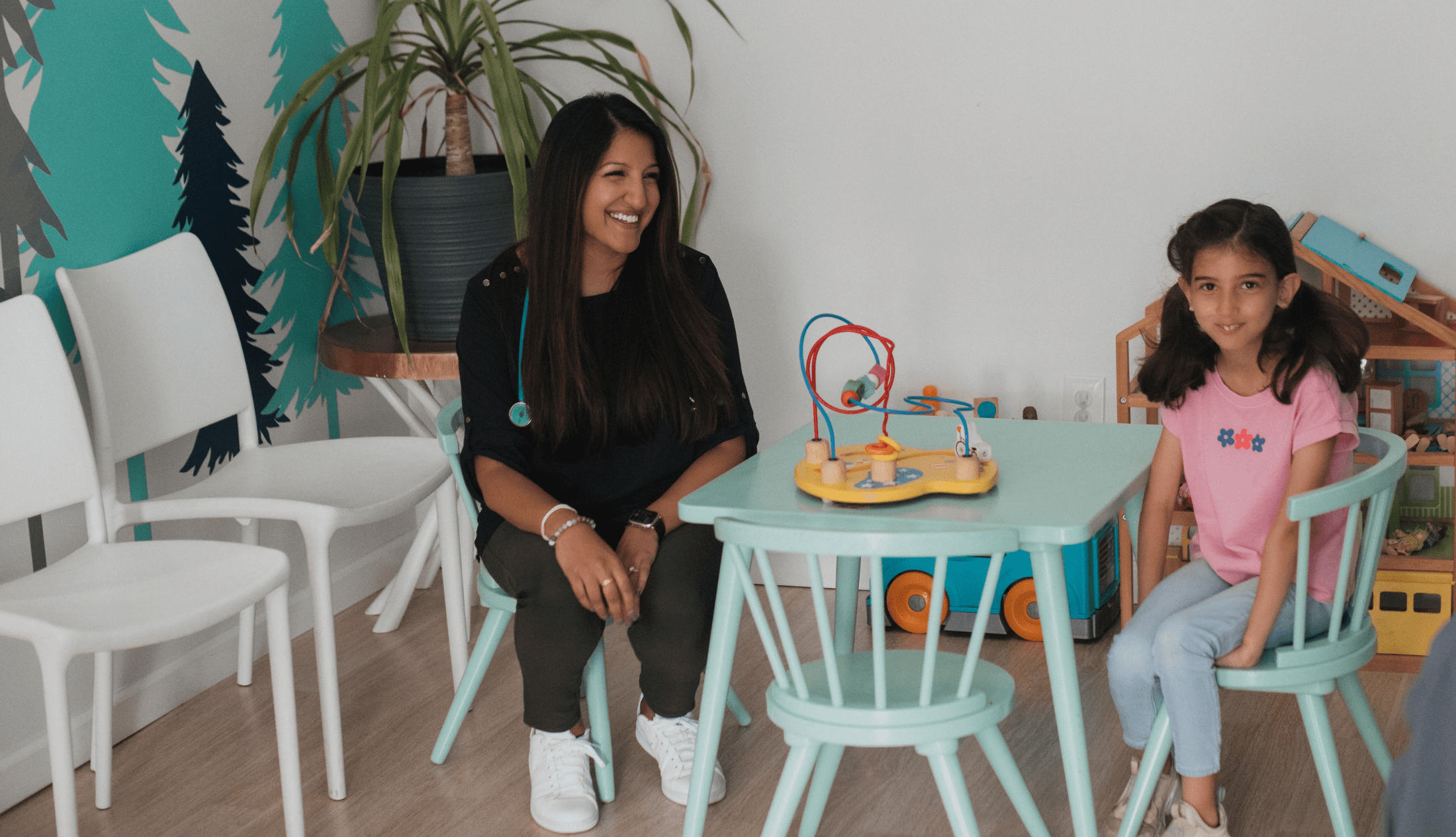 Dr Sonia Patel sitting on a kiddies table with a an adorable little girl sitting accross her at Rivertowns Pediatrics